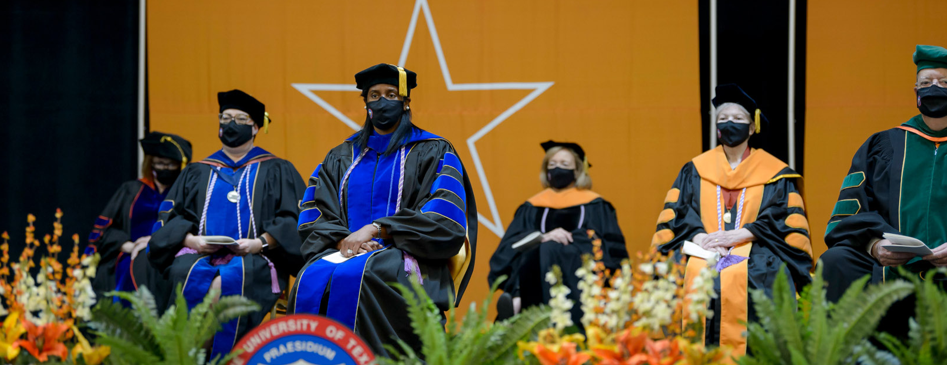 UTMB faculty on commencement stage in full regalia with flowers in foreground