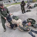 Military personnel in flight suits and protective gear participate in outdoor training.