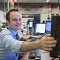 Man wearing a headset operates equipment at a console in a mission-control-style room.