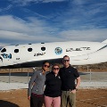 Three people stand in front of a Virgin Galactic spacecraft on display.