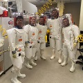Five people in white protective suits stand in a laboratory.