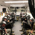 People in flight helmets and oxygen masks sit inside a hypobaric chamber.