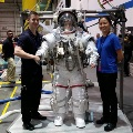 Two people stand beside a person wearing a spacesuit in a training facility.