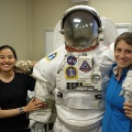 Two people pose beside an extravehicular mobility unit spacesuit.