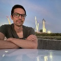 Person seated outdoors near a SpaceX Starship launch vehicle at dusk.