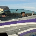 Two people wearing headsets sit in the cockpit of a small aircraft.