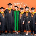 Six graduates in caps and gowns pose in front of a University of Texas Medical Branch backdrop.