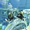 Two scuba divers swim among spaceflight-training hardware in a neutral buoyancy pool.