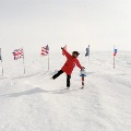 Person in a red parka stands at the South Pole among international flags.