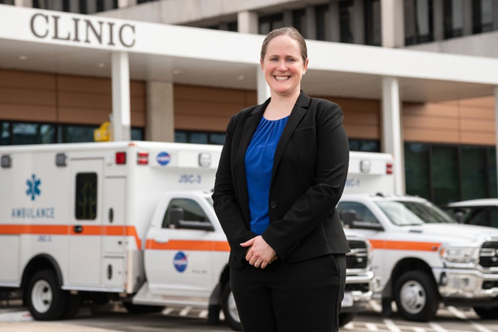 UTMB Aerospace & Exploration Medicine resident standing outside of the Johnson Space Center Clinic with two ambulances behind her  
