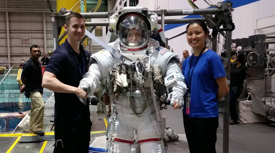 Two UTMB Aerospace Medicine residents stand beside a crew member wearing a spacesuit in a training facility.