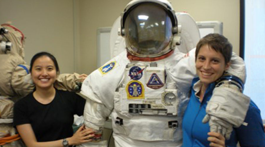 Two female UTMB Aerospace & Exploration Medicine residents standing with NASA’s Extra-vehicular Mobility Unit (EMU) spacesuit.