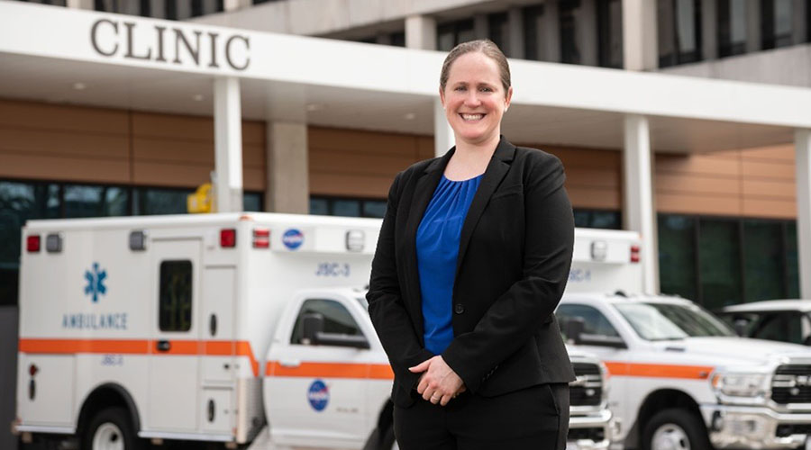 UTMB Aerospace & Exploration Medicine resident standing outside of the Johnson Space Center Clinic with two ambulances behind her.