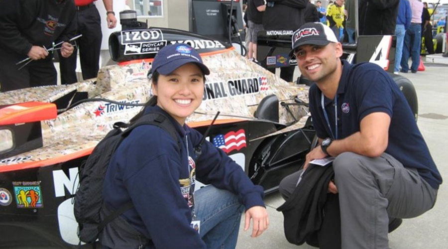 Two UTMB Aerospace Medicine residents crouching down next to an Indianapolis-500 race car while on their motorsport medicine rotation.