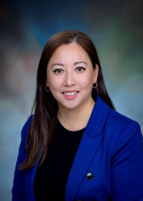 Studio portrait of a UTMB Medicine Services grants team staff member wearing a blue blazer over a dark top, positioned against a soft, neutral background.
