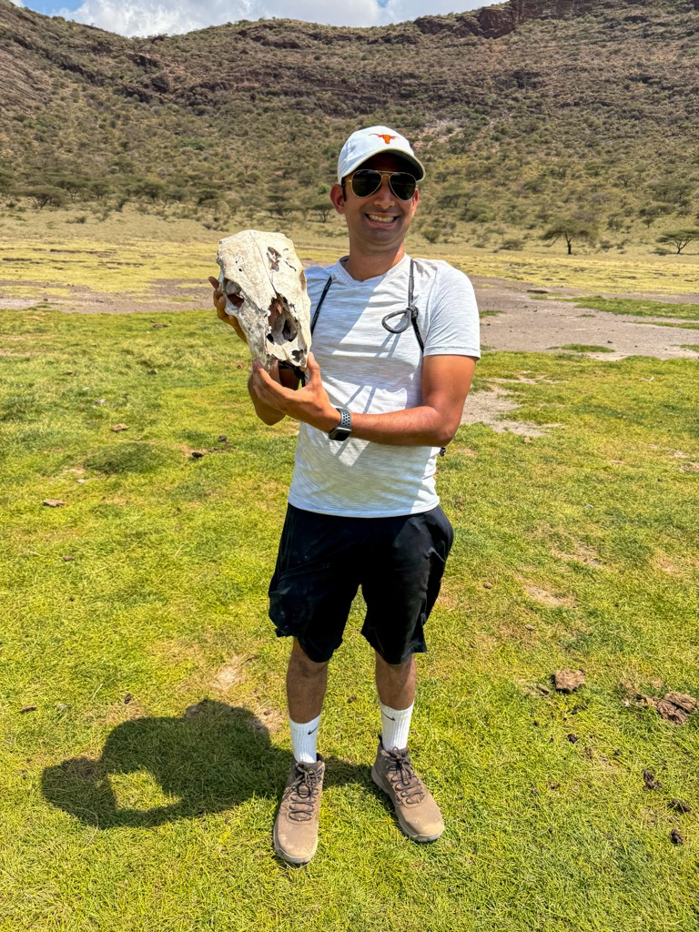 Man standing in the middle of a grassland in Kenya holding a skull from an animal.