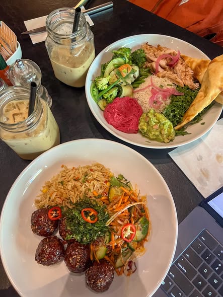 A table spread with colorful dishes at a Nairobi restaurant, including rice bowls, vegetables, falafel, and iced coffee drinks in mason jars