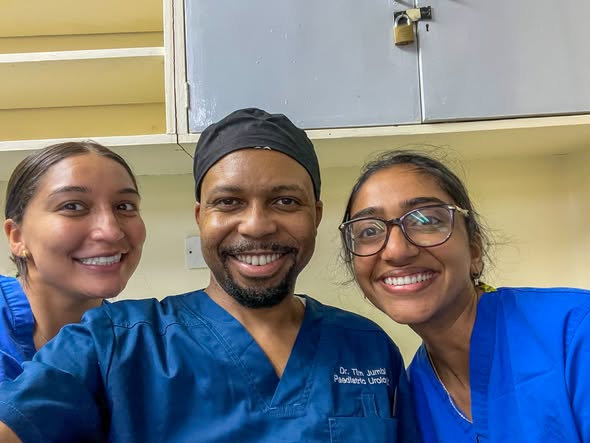 UTMB students Nidhi Subramanian and Zeyanna Dhalla in blue scrubs posing with a pediatric urologist at Kenyatta National Hospital during their clinical preceptorship.
