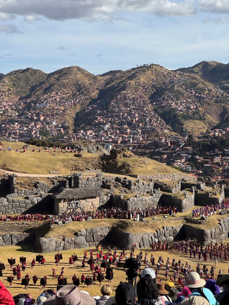 Fowler_6 A large crowd gathers in front of ancient stone ruins in a valley surrounded by mountains.