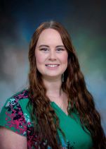 Professional headshot of Chelsea Tippit. Light complected woman with long, auburn hair and a green floral shirt smiling for a photo.