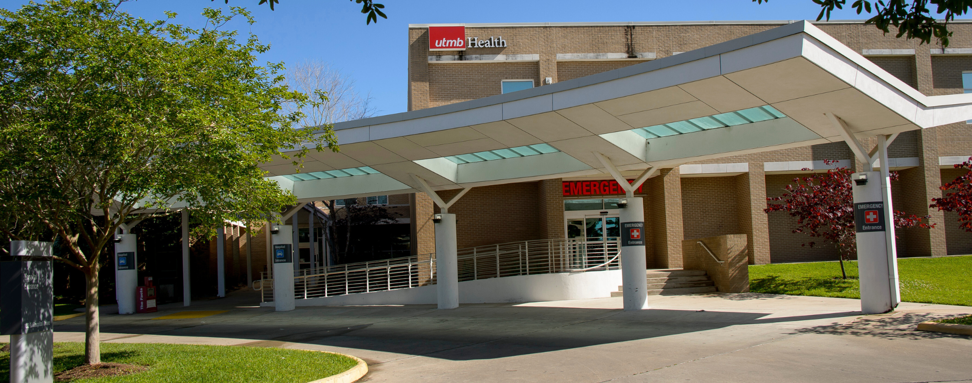 Exterior view of a UTMB Health building with a covered drop-off area and clearly marked emergency entrance doors.