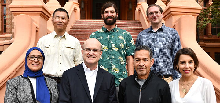 Small group of individuals in professional attire posing on outdoor brick steps in front of a historic campus building.