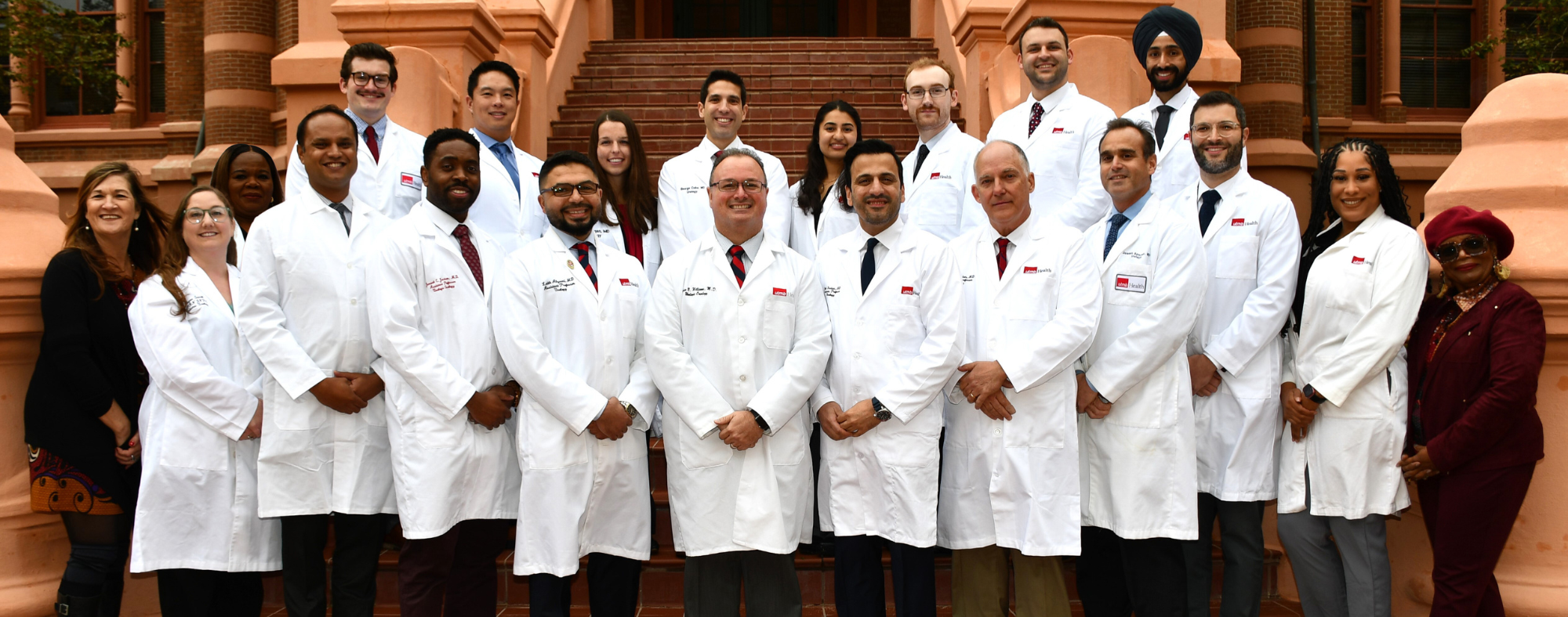 Group of medical professionals wearing white coats standing on outdoor steps in front of a historic brick building.