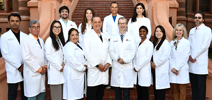 A large group of medical professionals in white coats stand together on outdoor steps in front of a campus building.