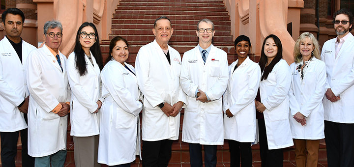 Group of medical professionals wearing white coats standing in a line on outdoor brick steps in front of a historic campus building.