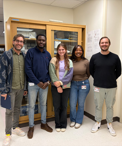 5 lab members, a diverse group of men and women smiling in a lab