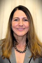 Headshot of Marjorie M. Cisneros smiling in a gray blazer in front of a light curtain backdrop.