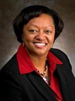Professional headshot of Beverly Echols wearing a black blazer and red collared shirt against a brown background.