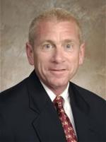 Professional headshot of Dr. Owen Murray wearing a dark suit jacket, white dress shirt, and patterned red tie against a neutral backdrop.