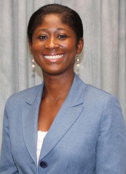 Professional headshot of Dr. Veronica Kwarteng‑Amaning wearing a light blue blazer, white top, and pearl drop earrings in front of a light gray curtain backdrop.
