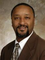 Professional headshot of Anthony Williams wearing a brown suit jacket, white shirt, and patterned tie against a neutral backdrop.