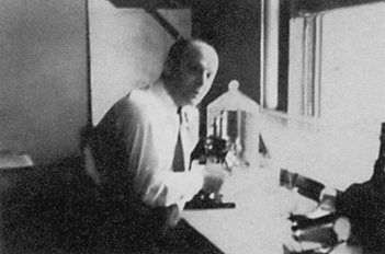 Elwood Baird poses for camera at his desk with a microscope.