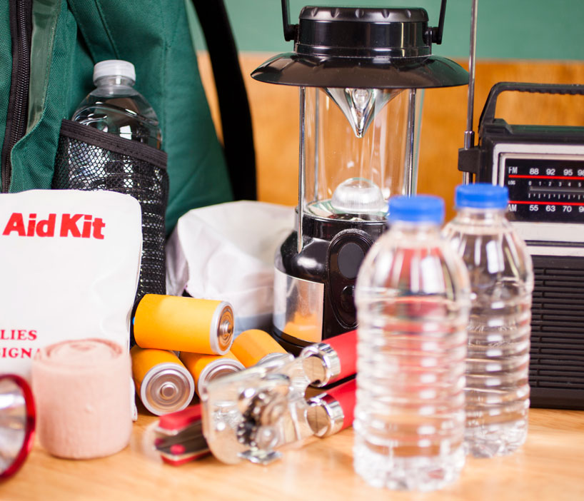Close up image of items needed to survive an emergency situation like a flashlight, water, batteries and a radio.