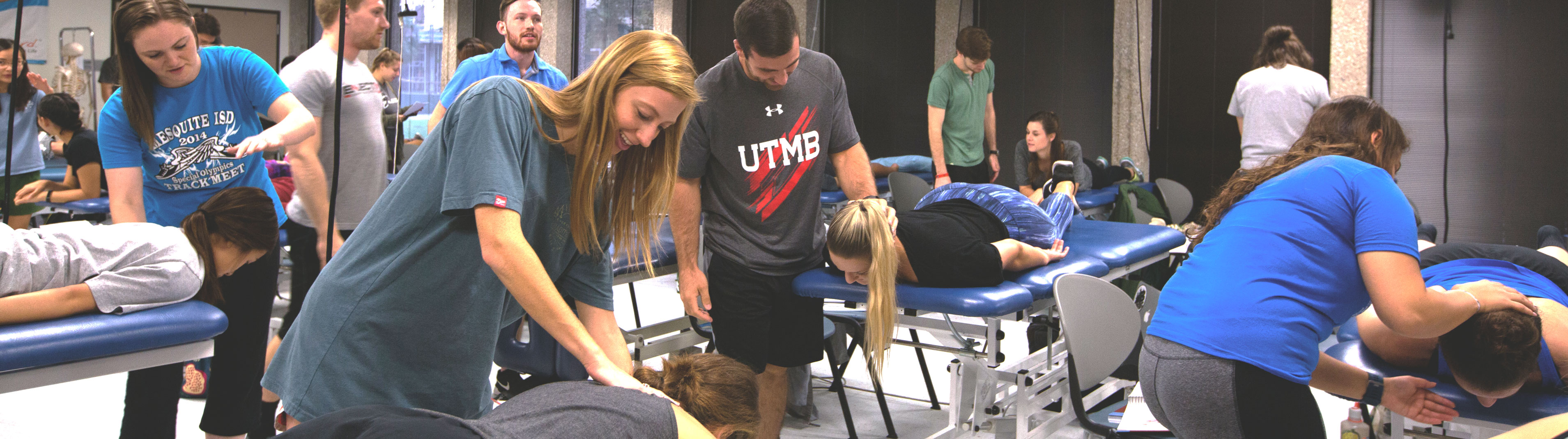 Group of students in a physical therapy lab, instructing other students who are practicing neck extensions on tables.