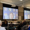 Group of guests listening to a guest speaker on the video screen