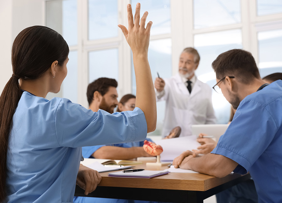 A respiratory therapy student raises her hand during a classroom lesson with an instructor and classmates.
