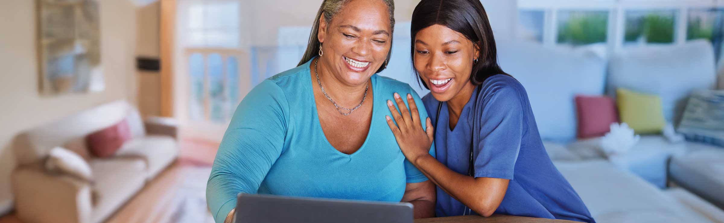 older woman of color at home with younger woman caretaker, using a laptop