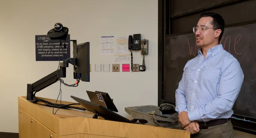 photo of Dr. Aparicio, a man wearing a collared shirt at a podium in a classroom