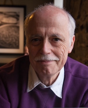 man wearing a sweater and collared shirt, smiling in a relaxed office setting