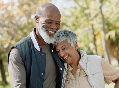 older adult couple, a man and woman of color, smiling outdoors while hugging