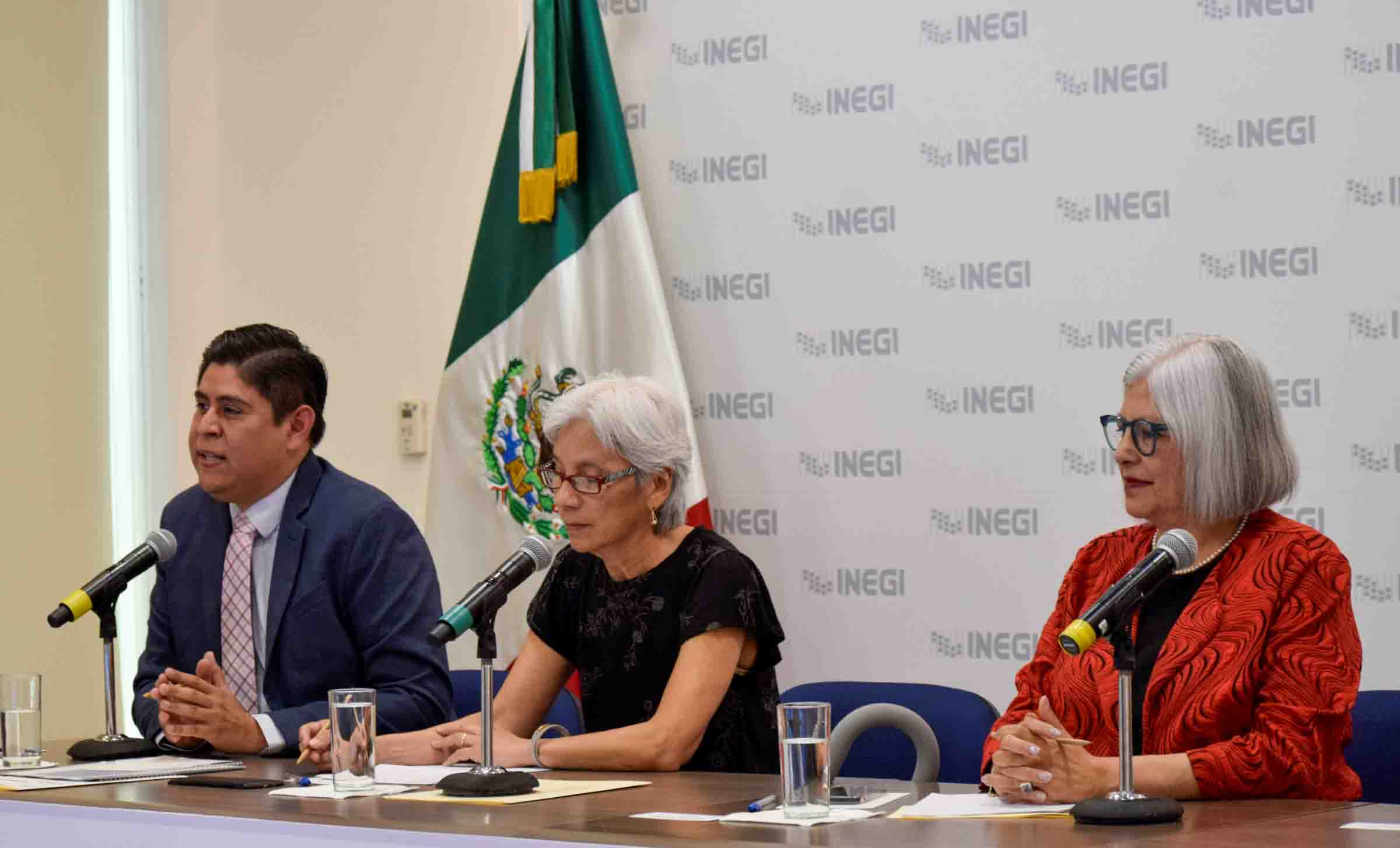 three researchers seated at table with microphones in front of Mexican flag