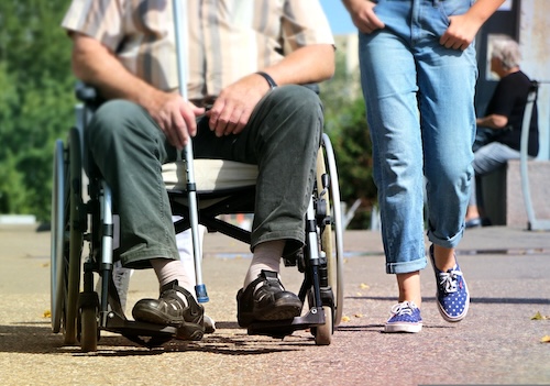 closeup of lower half of person using a wheel chair with another person walking beside them outdoors