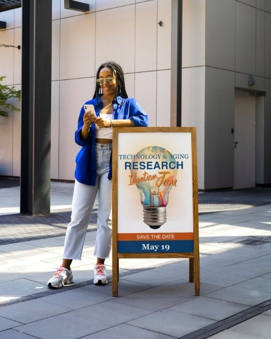 young woman of color leaning on a sign for a Research Jam on May 19