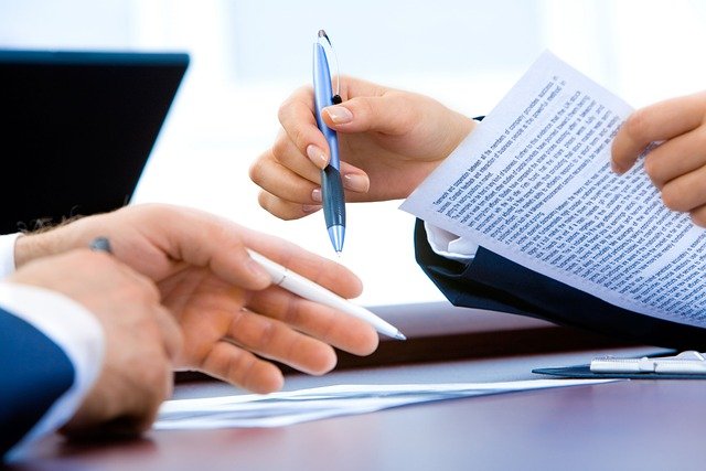 photo of two people's hands while reviewing documents and holding pens