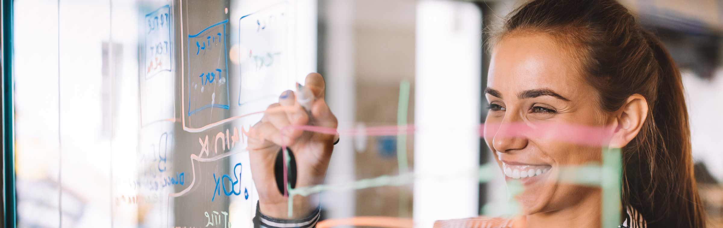 woman smiling while writing on a transparent board in an academic or office setting