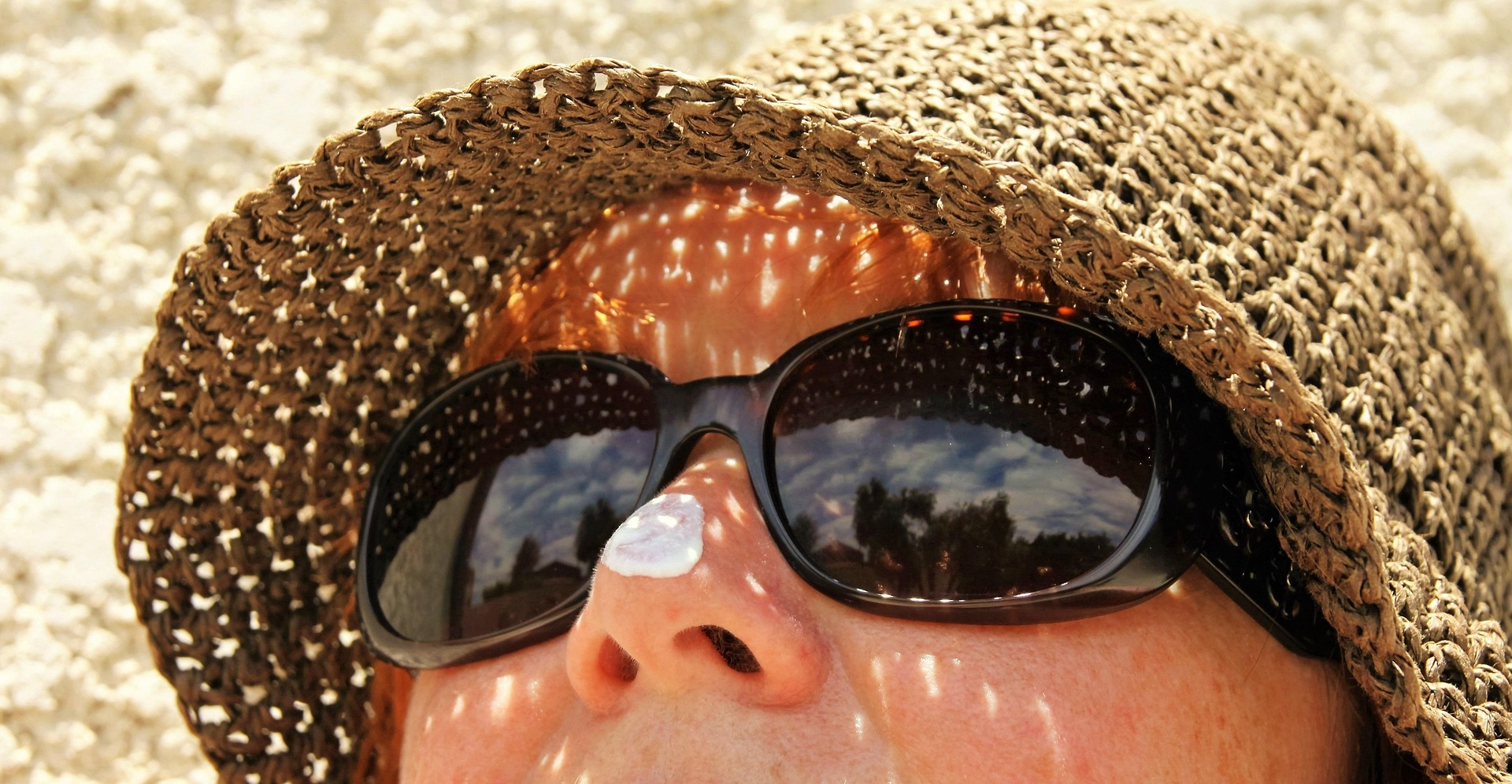 Person's face closeup, wearing hat and sunglasses with sunblock on nose.
